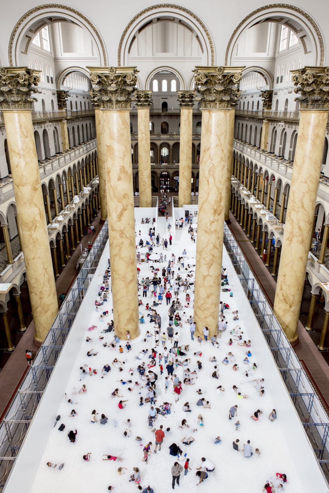 Vista aérea de The Beach, da Snarkitecture -- uma vasta piscina de bolinhas brancas preenchendo o salão colunado Great Hall do National Building Museum