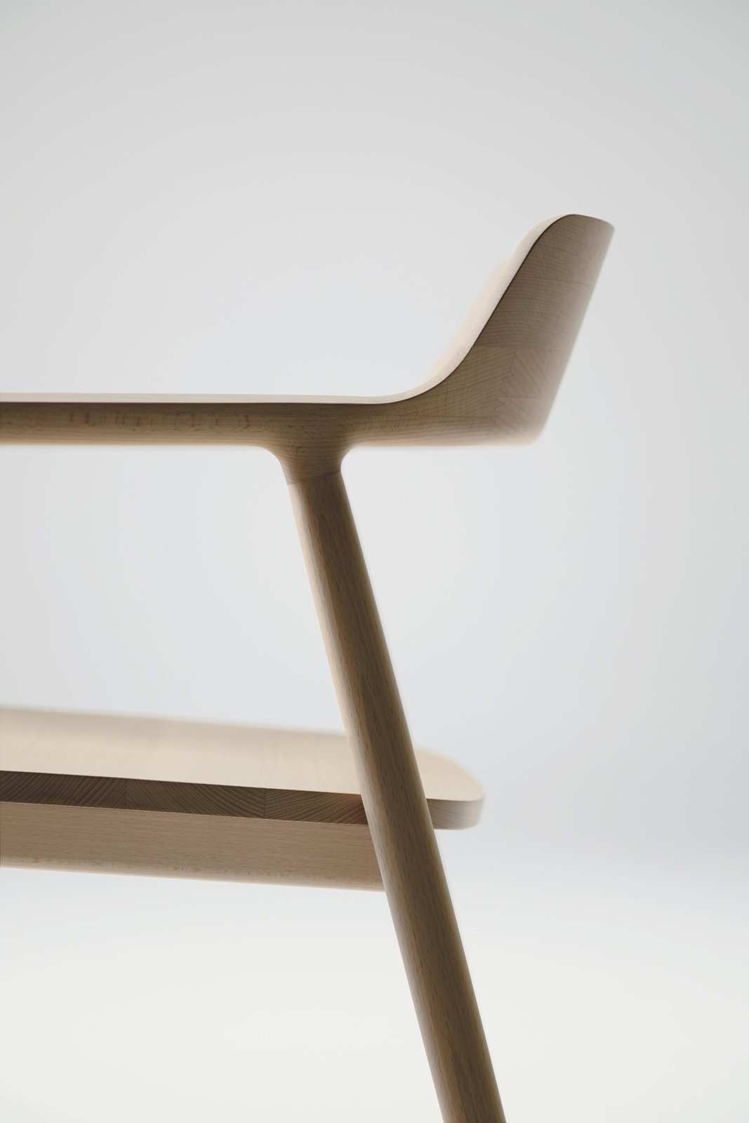 Detail of Maruni's Hiroshima armchair by Naoto Fukasawa, from the studio's own photography: pale beech in soft light, the arm flowing into the low backrest in one continuous carved line above the smooth seat
