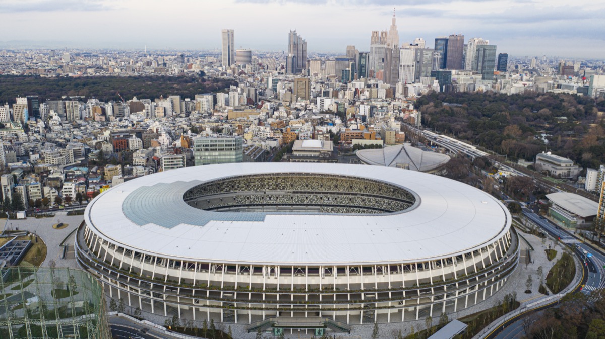 Japan National Stadium seen against the Shinjuku skyline, its low layered eaves holding the horizon