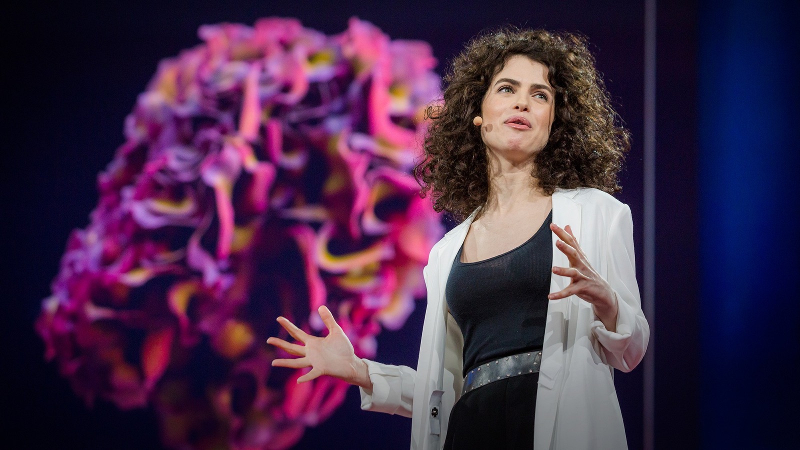 Neri Oxman discursando no TED em 2015, uma renderização colorida de uma de suas obras projetada atrás dela
