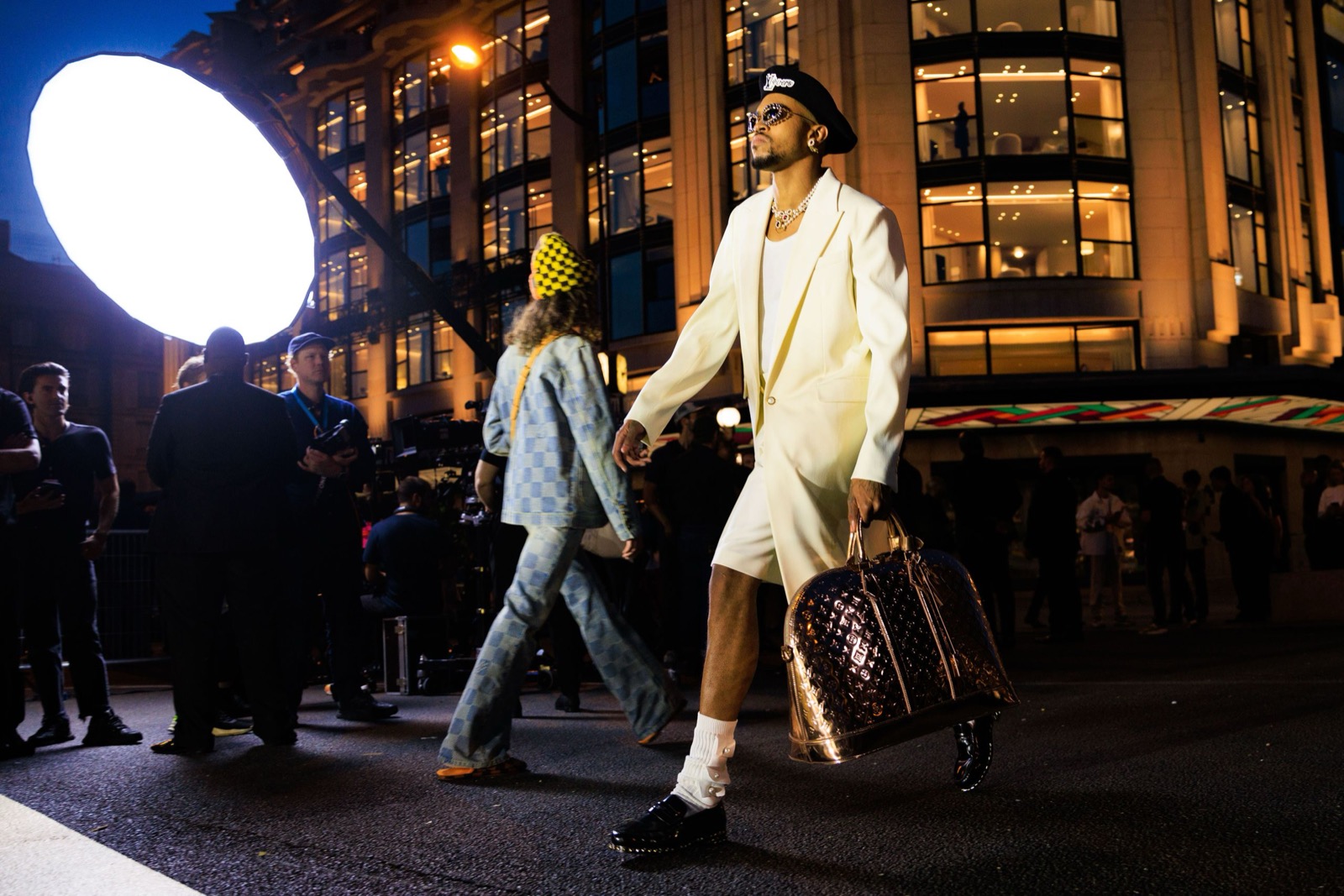 Pharrell Williams em um terno branco e boina com uma Keepall dourada da Louis Vuitton em seu desfile de estreia LV SS24 na Pont Neuf, Paris