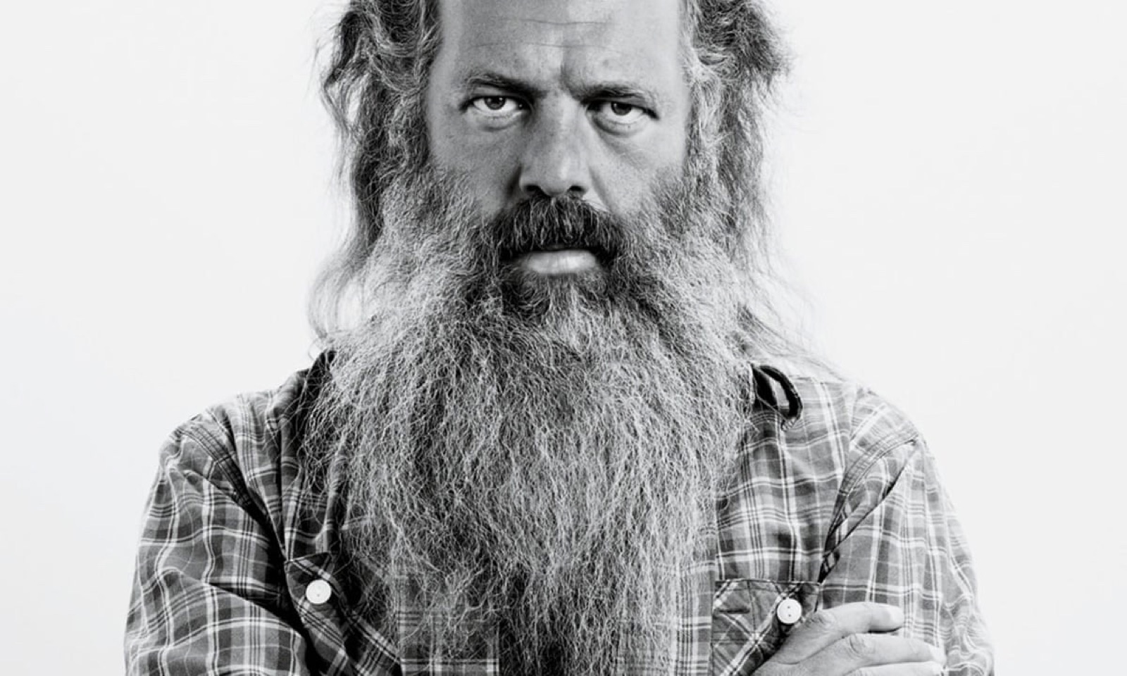 Schwarz-Weiß-Porträt von Rick Rubin mit verschränkten Armen, mit seinem ikonischen langen grauen Bart und Karohemd vor weißem Hintergrund