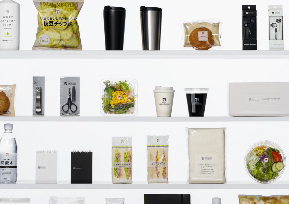Lineup das embalagens de marca própria da 7-Eleven Japan redesenhadas por Sato -- salgadinhos, bebidas, copos de café, sanduíches e produtos domésticos compartilhando um sistema visual minimalista nas prateleiras