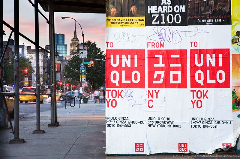 Cartaz de rua da inauguração da UNIQLO SoHo NYC (2006) mostrando o logo vermelho em inglês e katakana -- "TO UNIQLO TOKYO / FROM NYC / TO UNIQLO TOKYO" -- com o Empire State Building visível ao fundo de uma rua de Manhattan