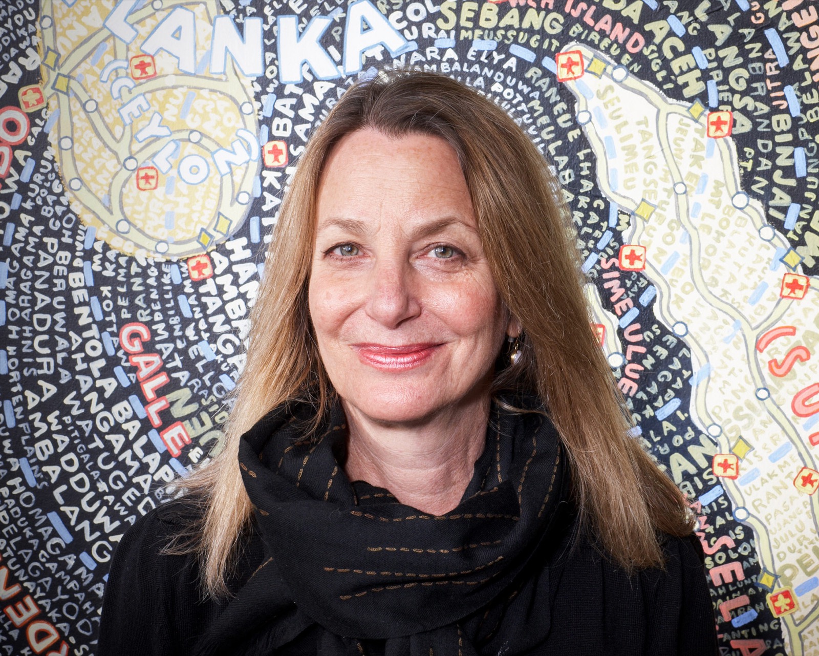Paula Scher fotografiada frente a una de sus pinturas-mapa tipográficas pintadas a mano