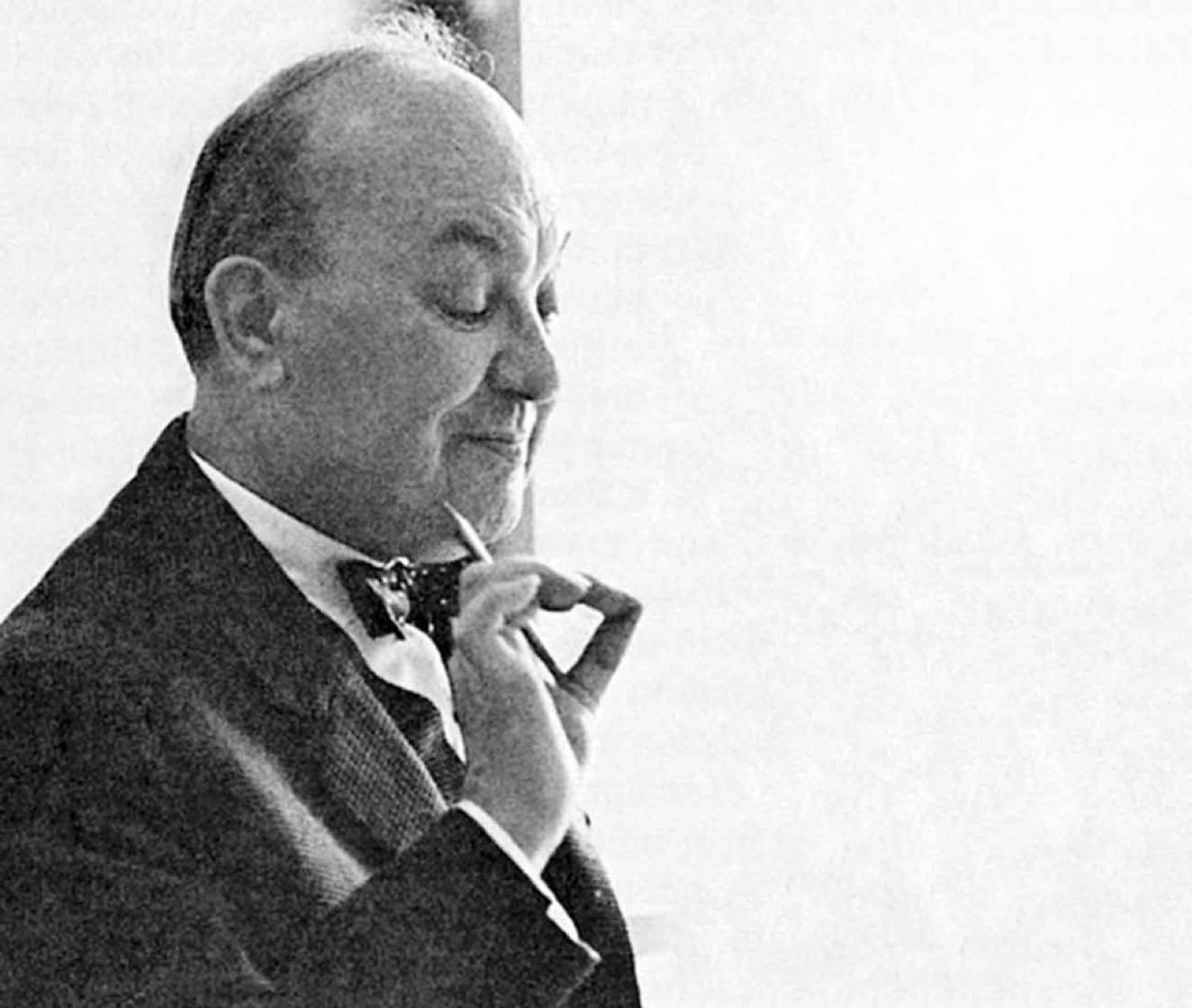 Jan Tschichold de perfil, con pajarita, sosteniendo sus gafas en una pose contemplativa