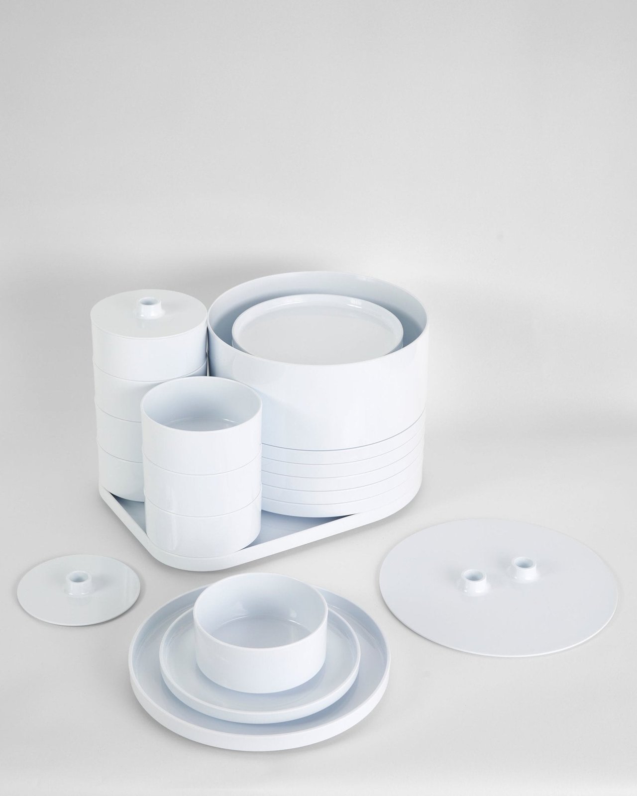 Massimo and Lella Vignelli's Max 1 dinnerware for Heller: glossy white molded melamine plates, bowls, and cups nested into compact cylindrical stacks on their tray, with a single place setting and flat lids arranged in front